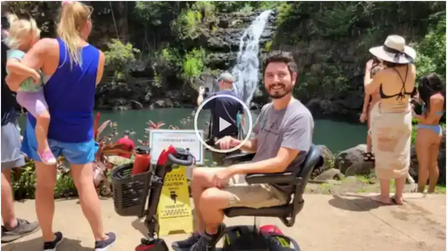 Video: traveler using a power wheelchair beside Waimea Falls, with other visitors nearby